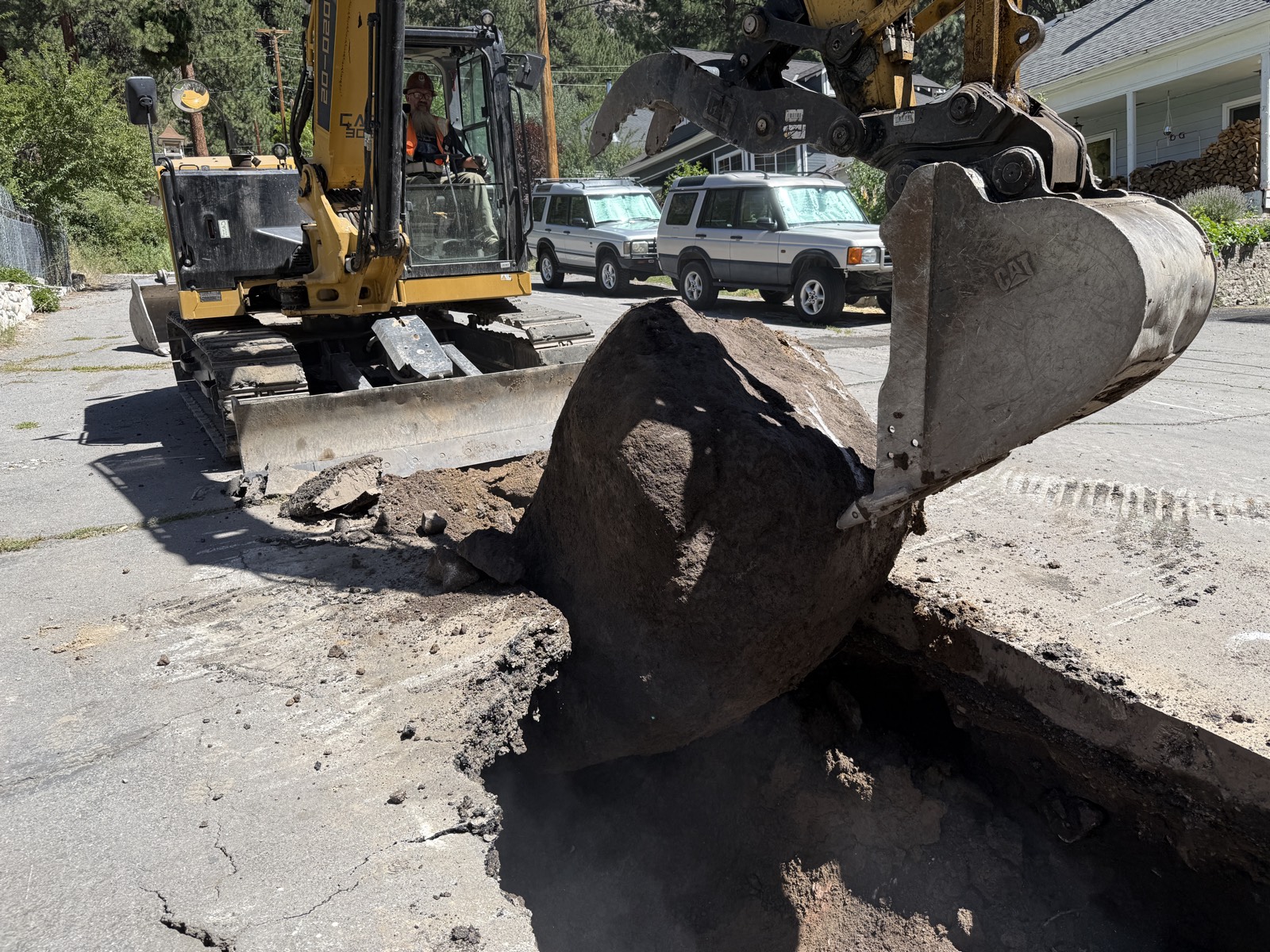 CAT excavator lifting a boulder out of a utility trench cut through old pavement on a Truckee jobsite