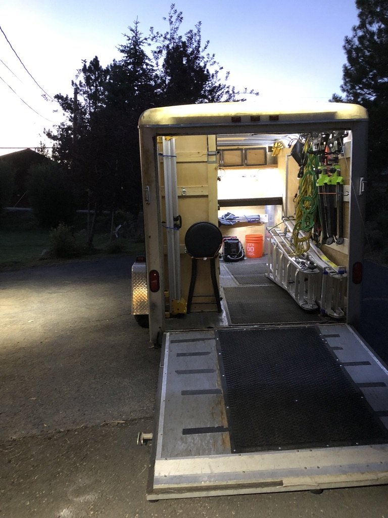 Golden-hour exterior reveal of the finished mobile carpentry trailer — ramp down, interior glowing warm, Sierra mountain silhouette in the background, Truckee CA, July 2018