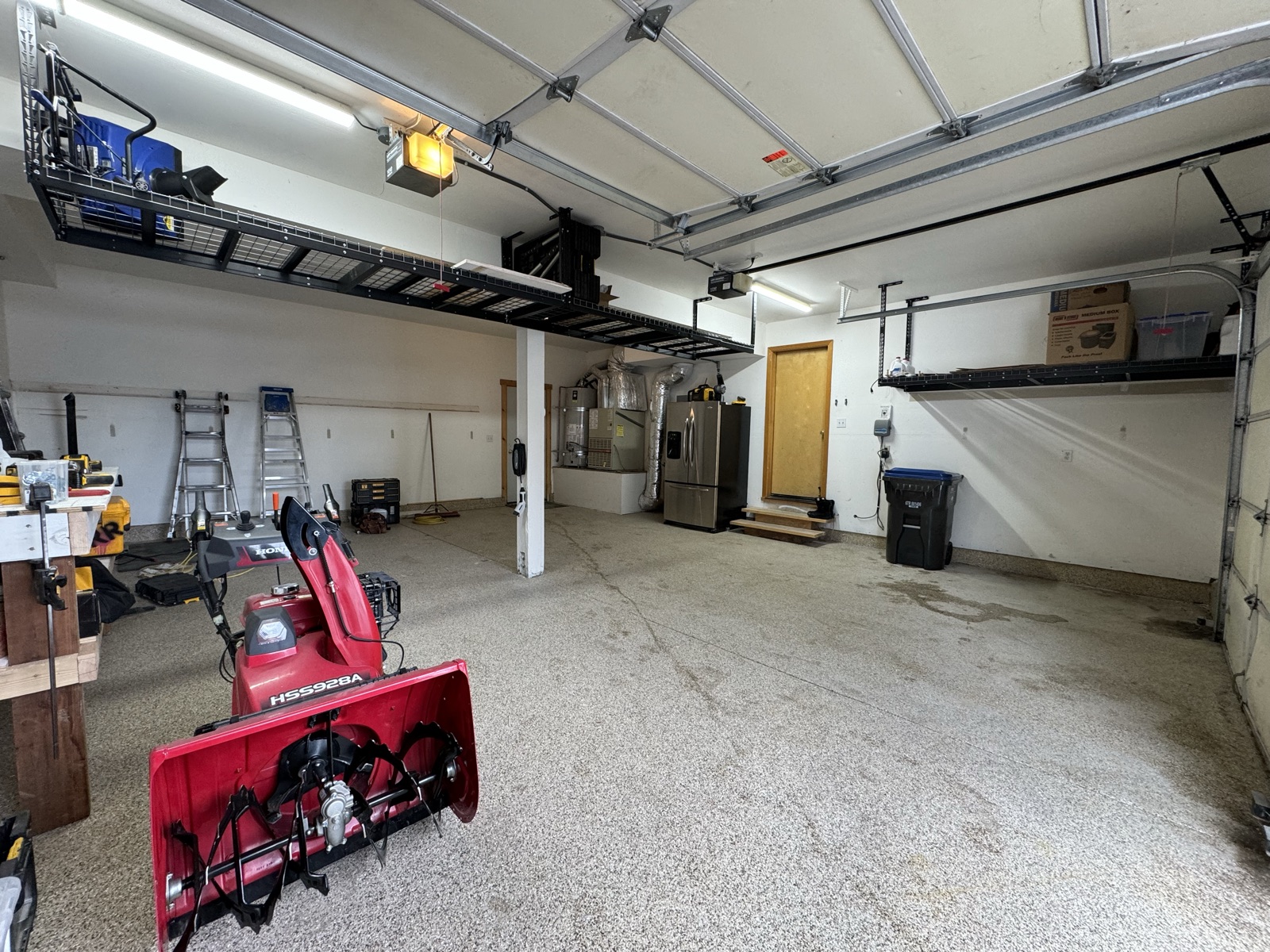 Wide interior shot showing overhead wire-rack storage installed across both bays with snowblower visible