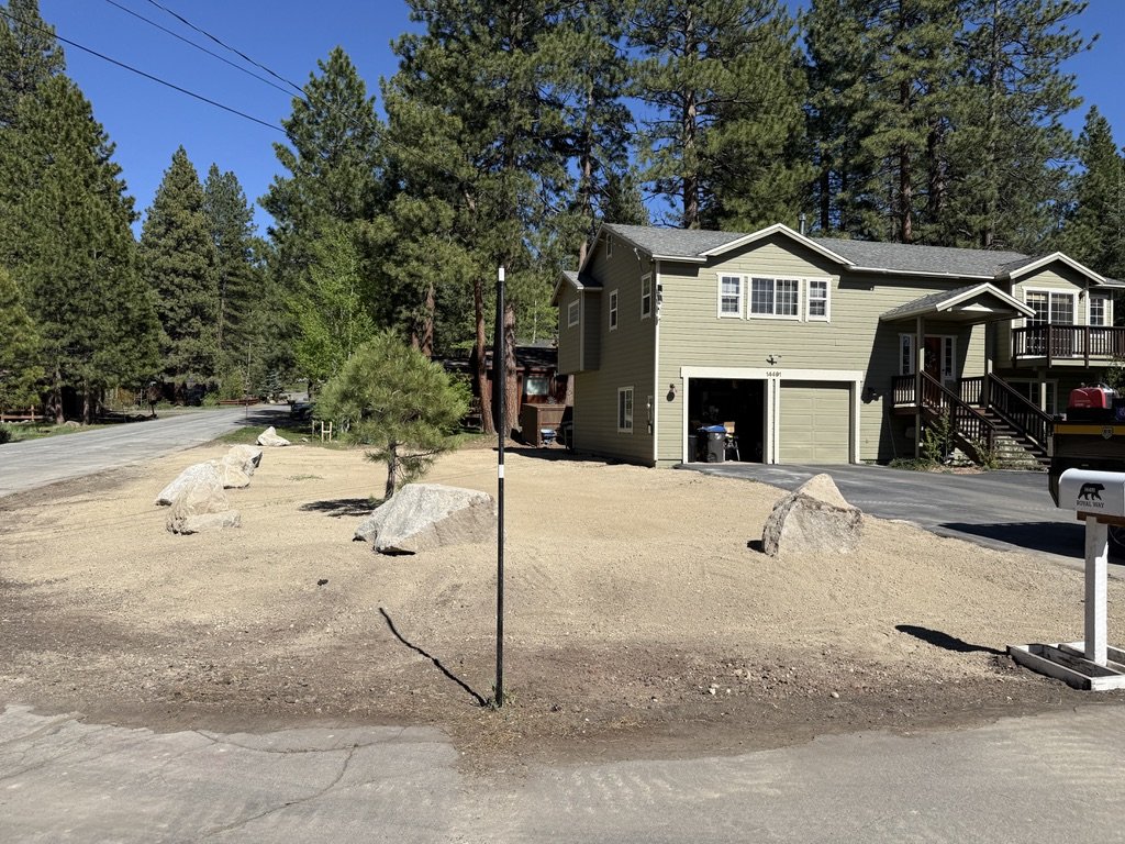 Sierra side yard reclamation — finished landscape with granite boulder retaining feature in front of white Truckee home, May 2026