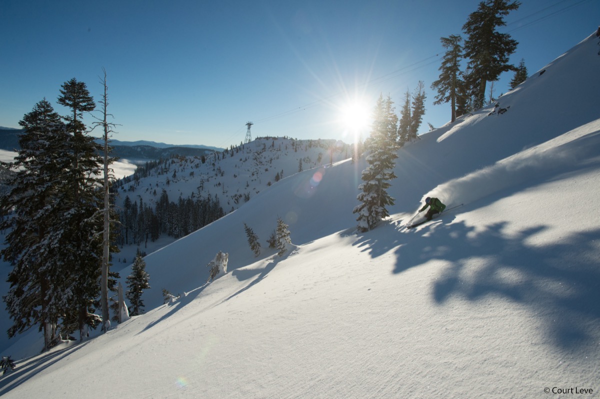 Errol skiing powder through trees in the Sierra Nevada with sunburst lighting